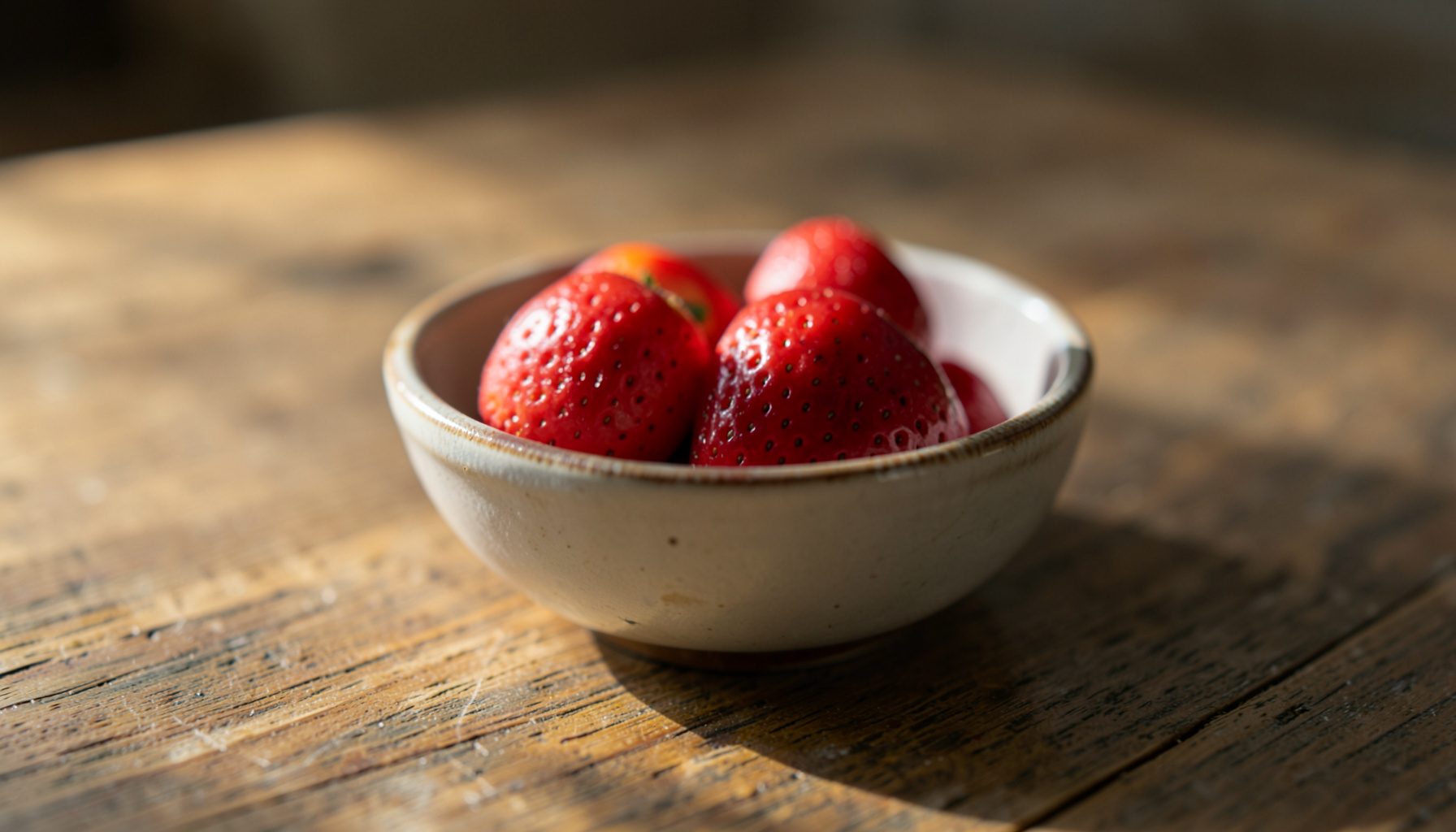 Soft natural light falling across a wooden tabletop with a simple ceramic bowl of fresh fruit, warm earthy tones