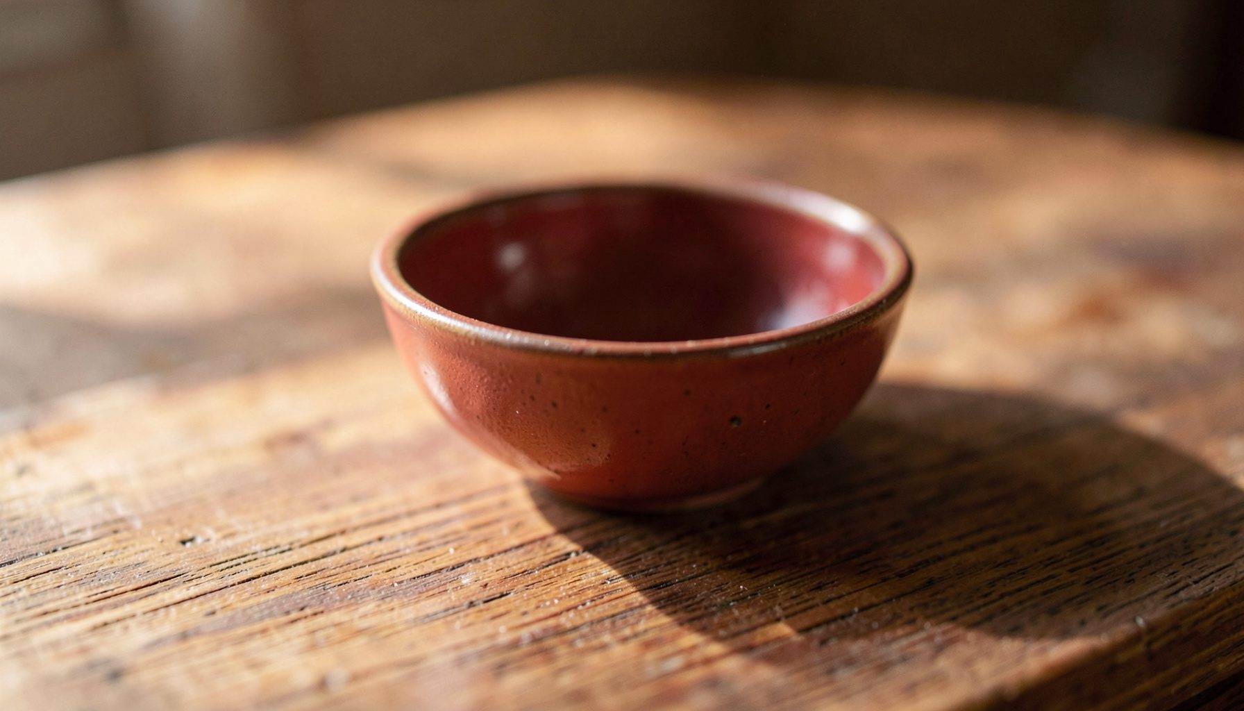Soft natural light falling across a wooden tabletop with a simple ceramic bowl, warm earth tones and gentle shadows